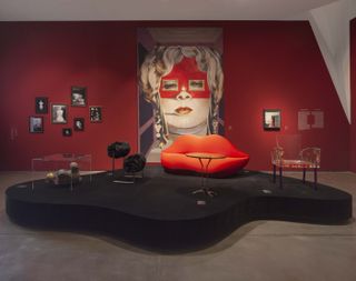 Red room with pictures on the wall and a black stage with red lip sofa on