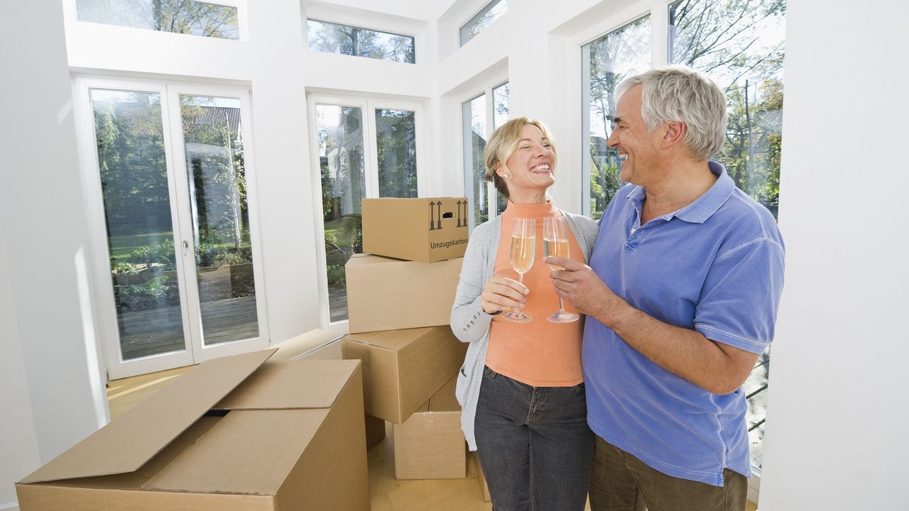 A very happy older couple share a toast amid piles of moving boxes.