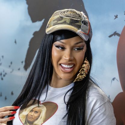 Cardi B wearing baseball cap in front of blue background