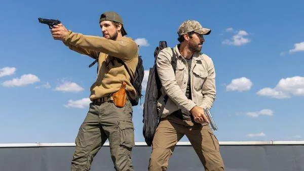 A still from the movie Take Cover in which two of the characters are holding up guns around them