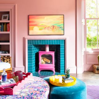 A pink-painted living room with a bobbin fireplace tiled in turquoise tiles, fitted with a pink wood burning stove and an artwork hanging above it