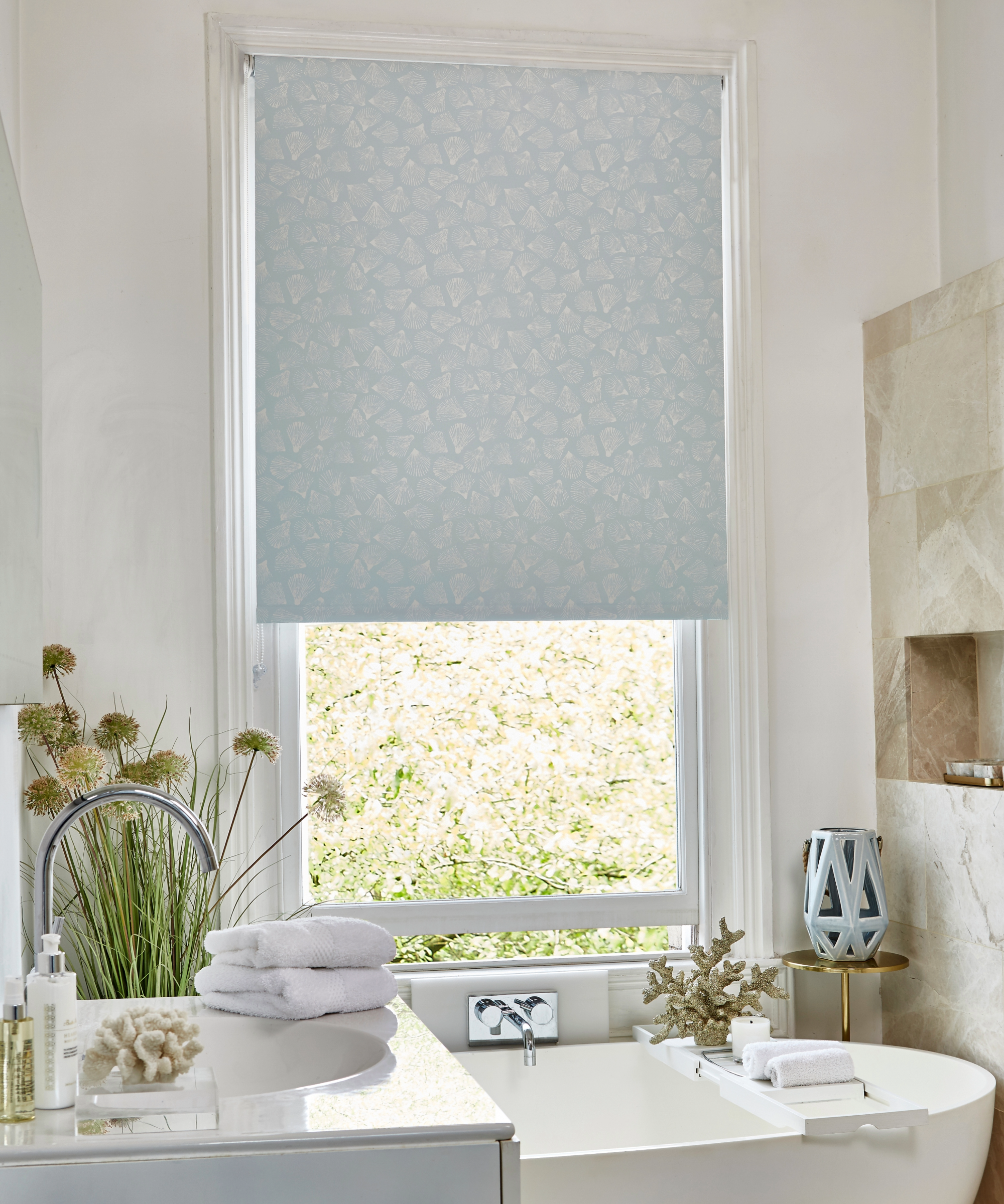 Blue bathroom with blue floral roller blinds, freestanding bath and flowers