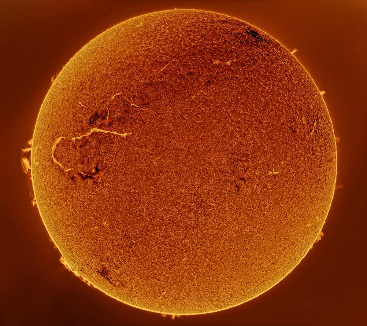 A bright orange sun fill the image. A large solar flare streaks like a scar across the star’s left side