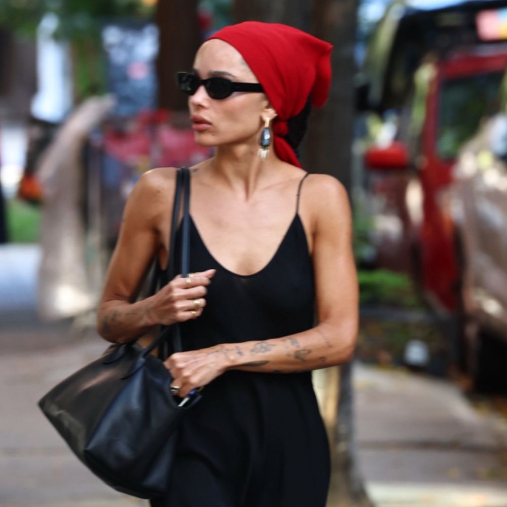 Zoe Kravitz walks down the street wearing a black slip dress with a red bandana, black flip-flops, a black leather bag and oversized earrings.