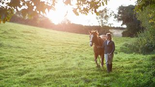 woman leading horse in grassy field towards the camera