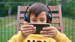 A child streams content on his phone while wearing headphones.