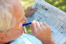 An older man works on a puzzle in his newspaper