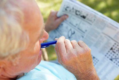An older man works on a puzzle in his newspaper