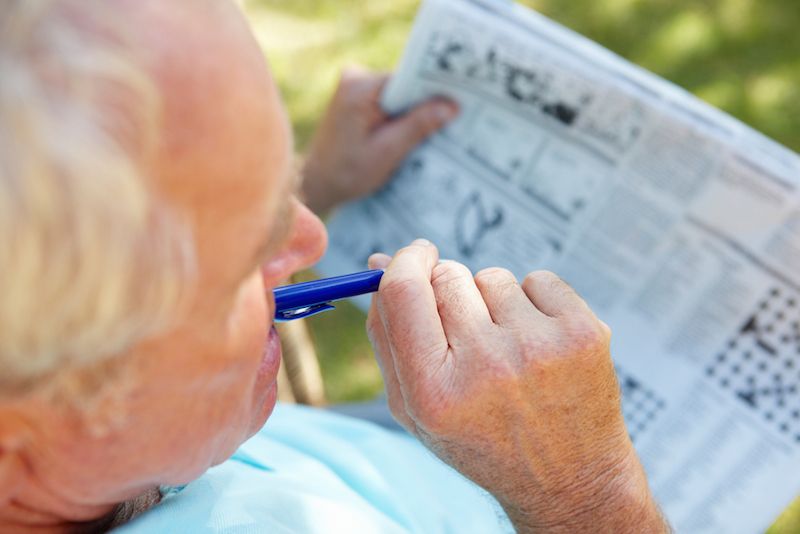 An older man works on a puzzle in his newspaper