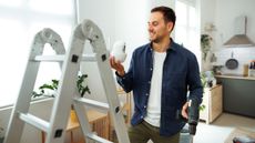 Man with stepladder and electric drill installing home security camera