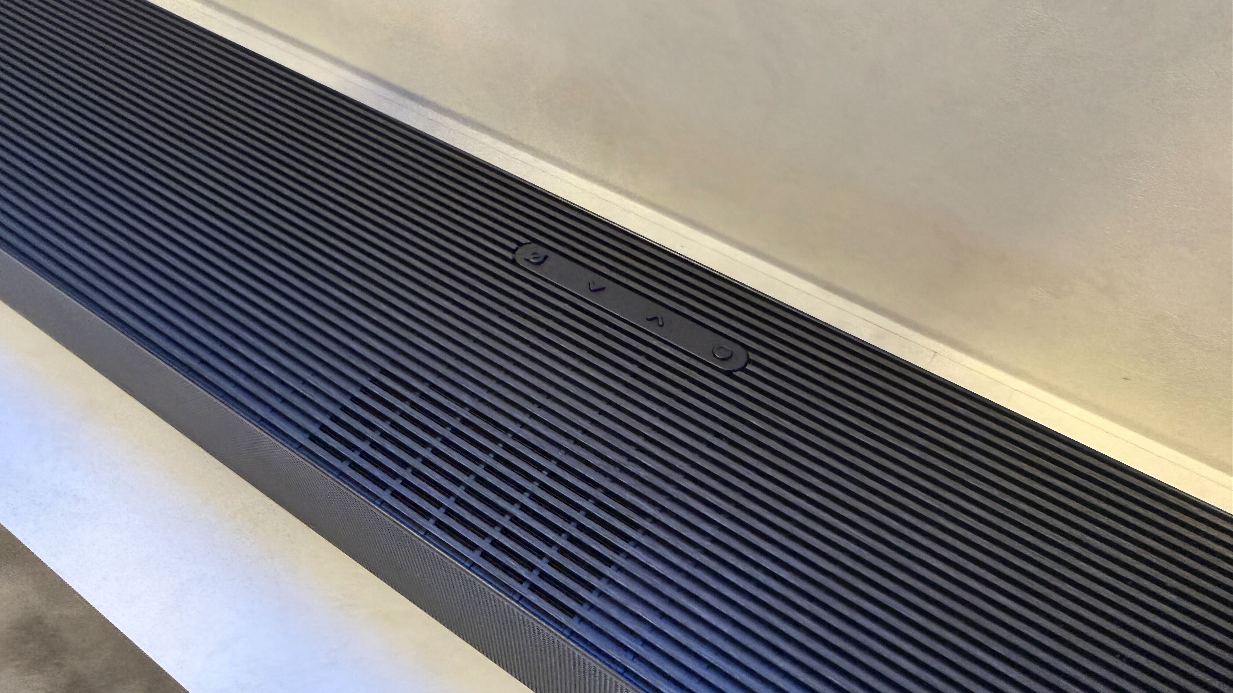 Samsung's HW-QS90H sitting below a wall-mounted TV on a white backdrop