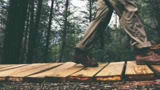 Walking boots vs walking shoes: a person wears dark brown walking boots to walk across a boardwalk in the forest