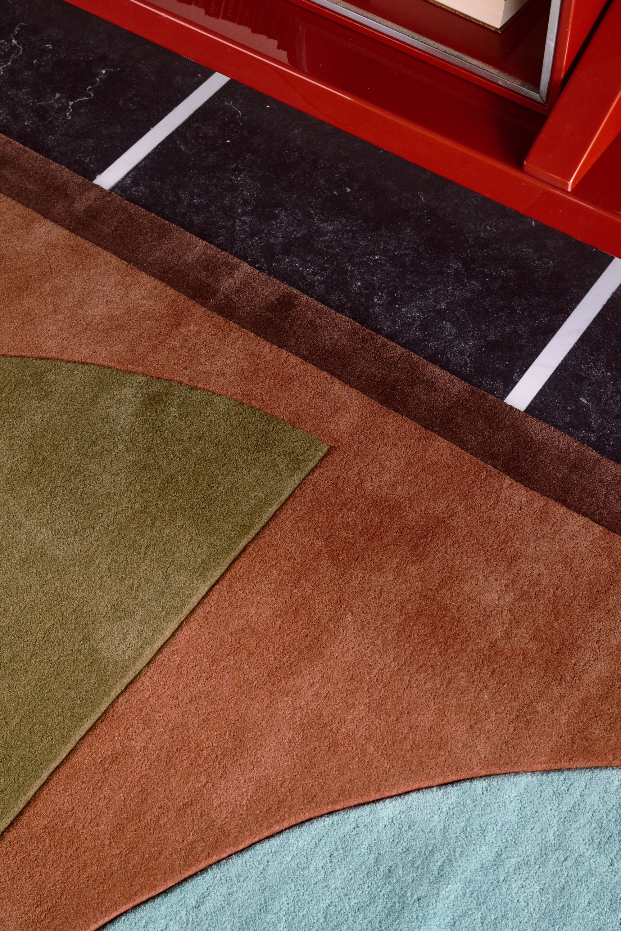 Close-up image of a terracotta-colored rug with brown trim and green and blue shapes in it.