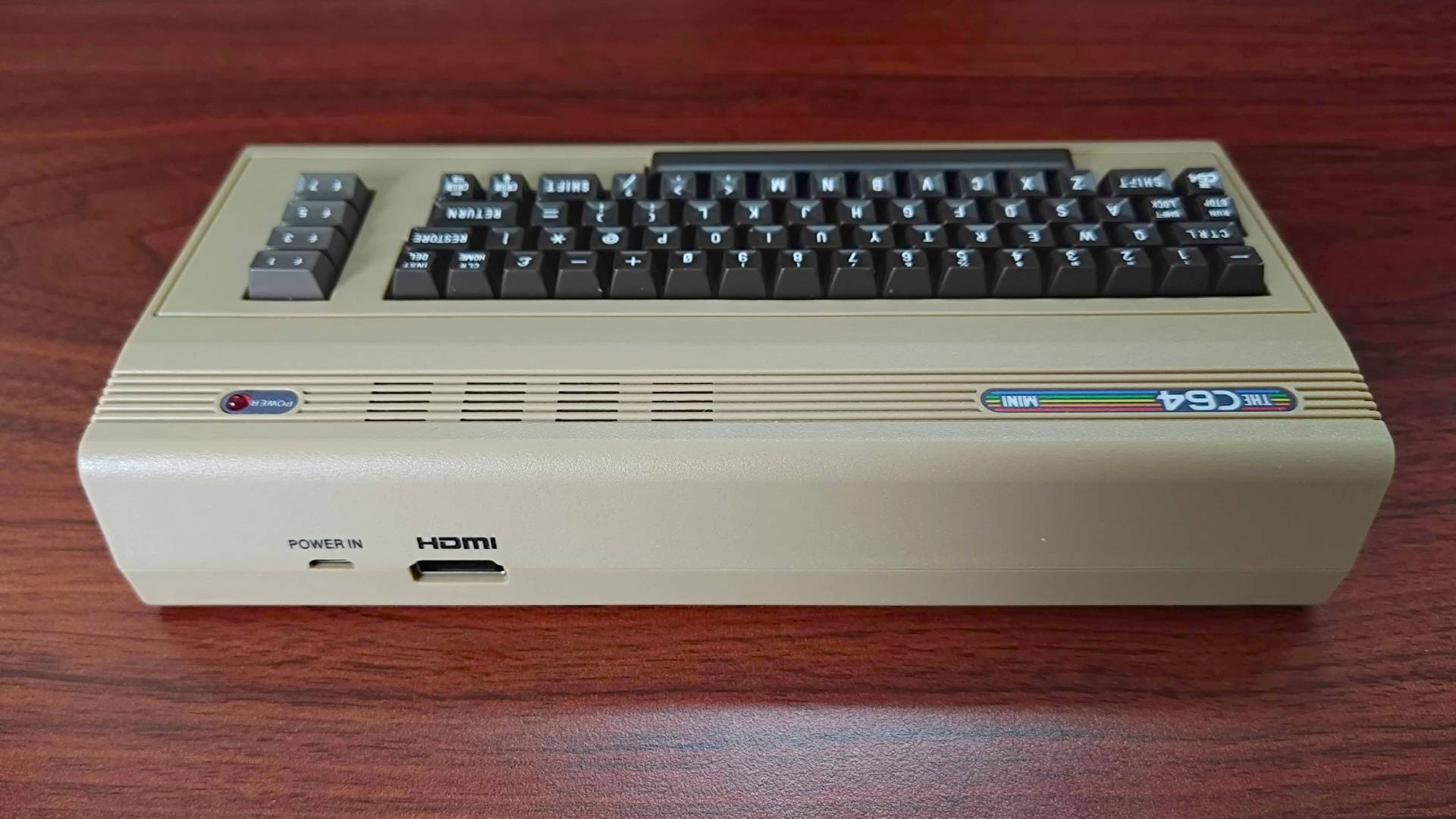 Back view of The C64 Mini on woodgrain desk with power and HDMI ports in view.