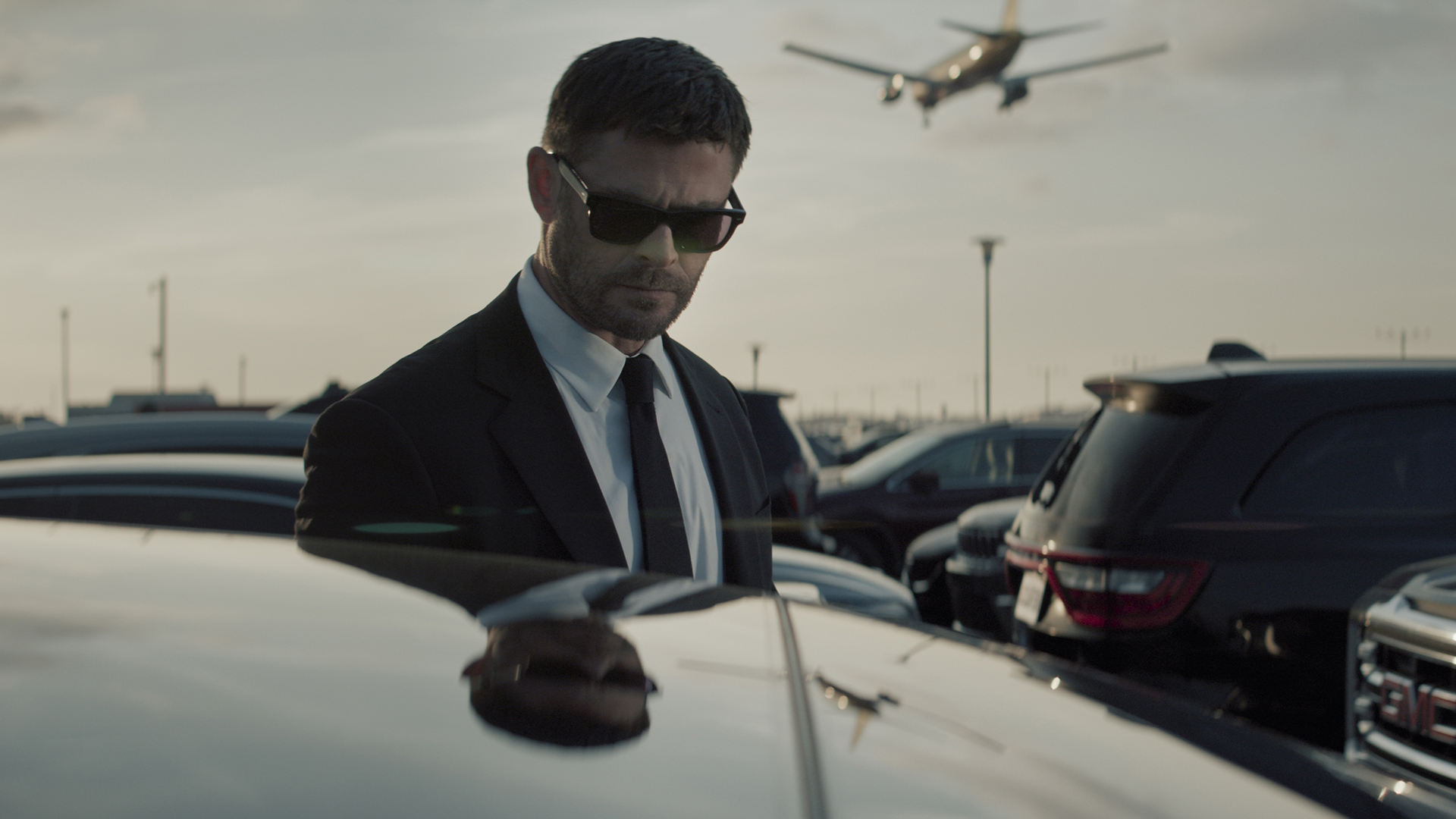 Mike Davis standing next to a car while wearing sunglasses and a suit in Crime 101
