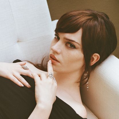 Image of Sophie Thatcher laying on couch wearing a black off the shoulder dress