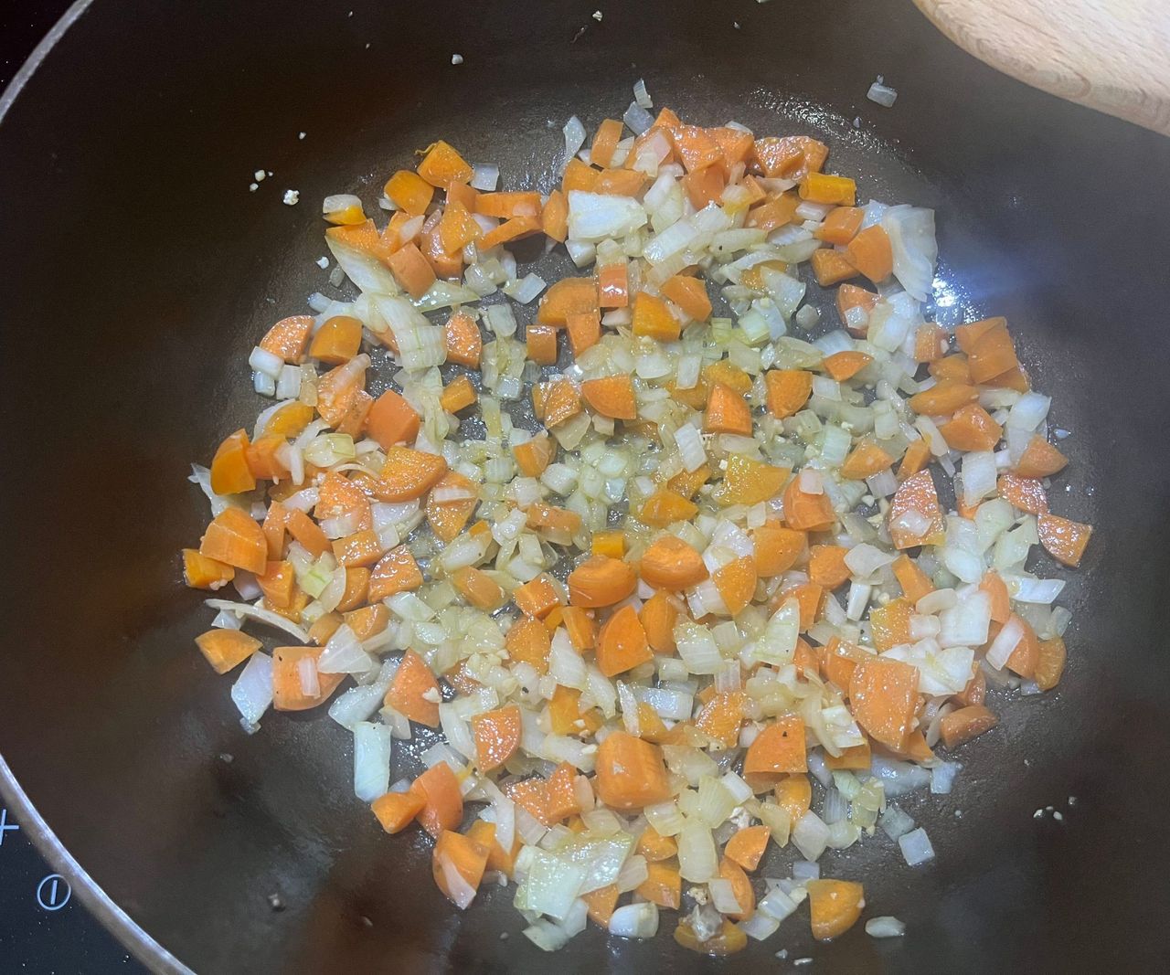A small bronze colored cast-iron Dutch oven with onions and carrots finely diced inside.