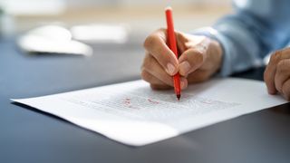 A hand holding a red pen corrects writing on a piece of paper.