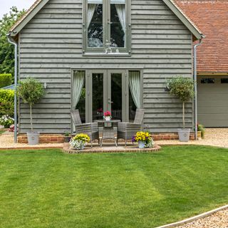 Neat green grass lawn behind house with rattan seating area on gravel