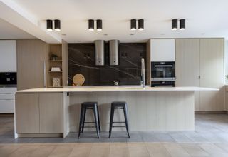 A modern kitchen with kitchen island, black bar stools and two cylinder extractor fans