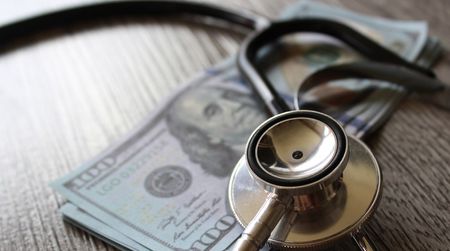 Stethoscope and money on a wooden table.