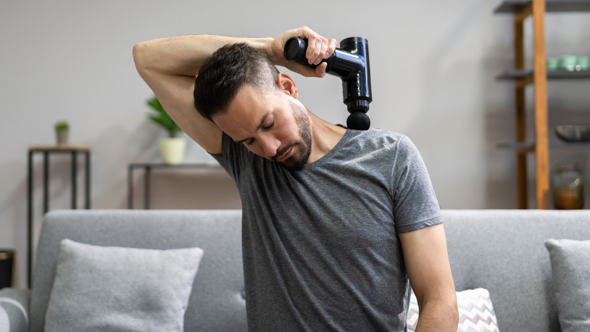 man using a massage gun to relieve pain in his shoulders