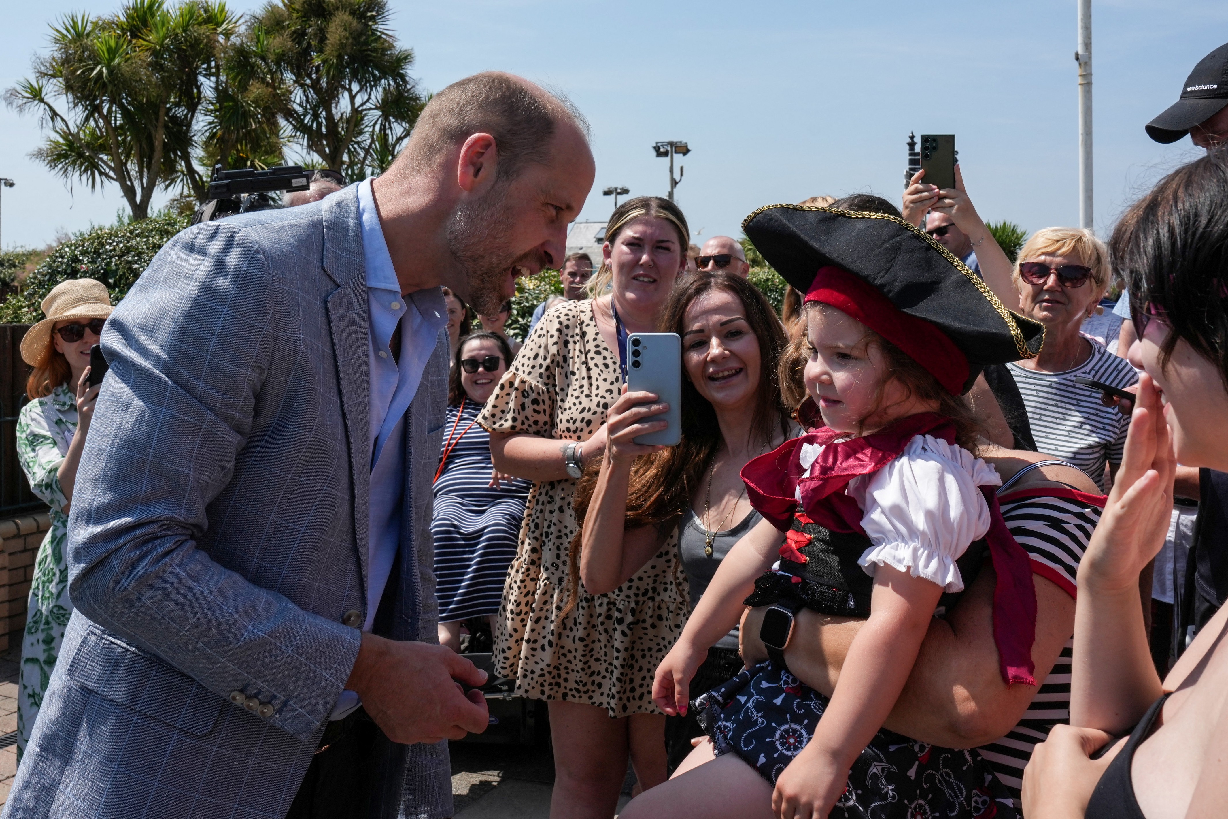 Prince William wears a gray suit jacket, a blue shirt and black slacks to visit Hastings, where he meets children and royal fans on the seafront