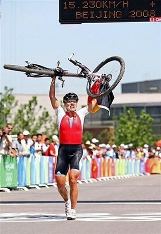 Sabine Spitz of Germany crosses the line in first carrying her bike and the German flag over the line at the 2008 Olympic Games cross country mountain bike race.