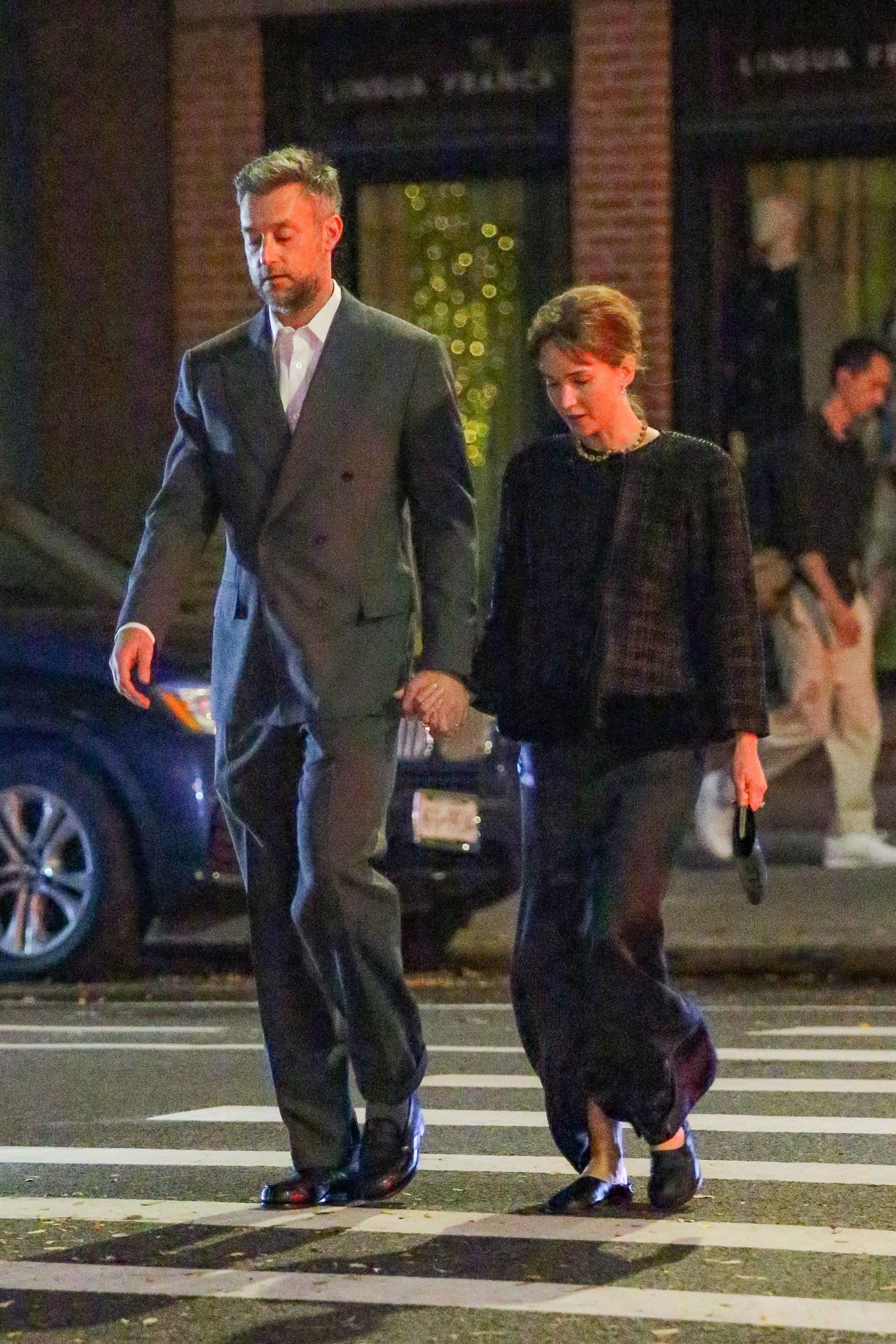 Jennifer Lawrences crosses the street holding hands with her husband. She wears a black satin maxi dress with a black tweed jacket and black slipper flats.