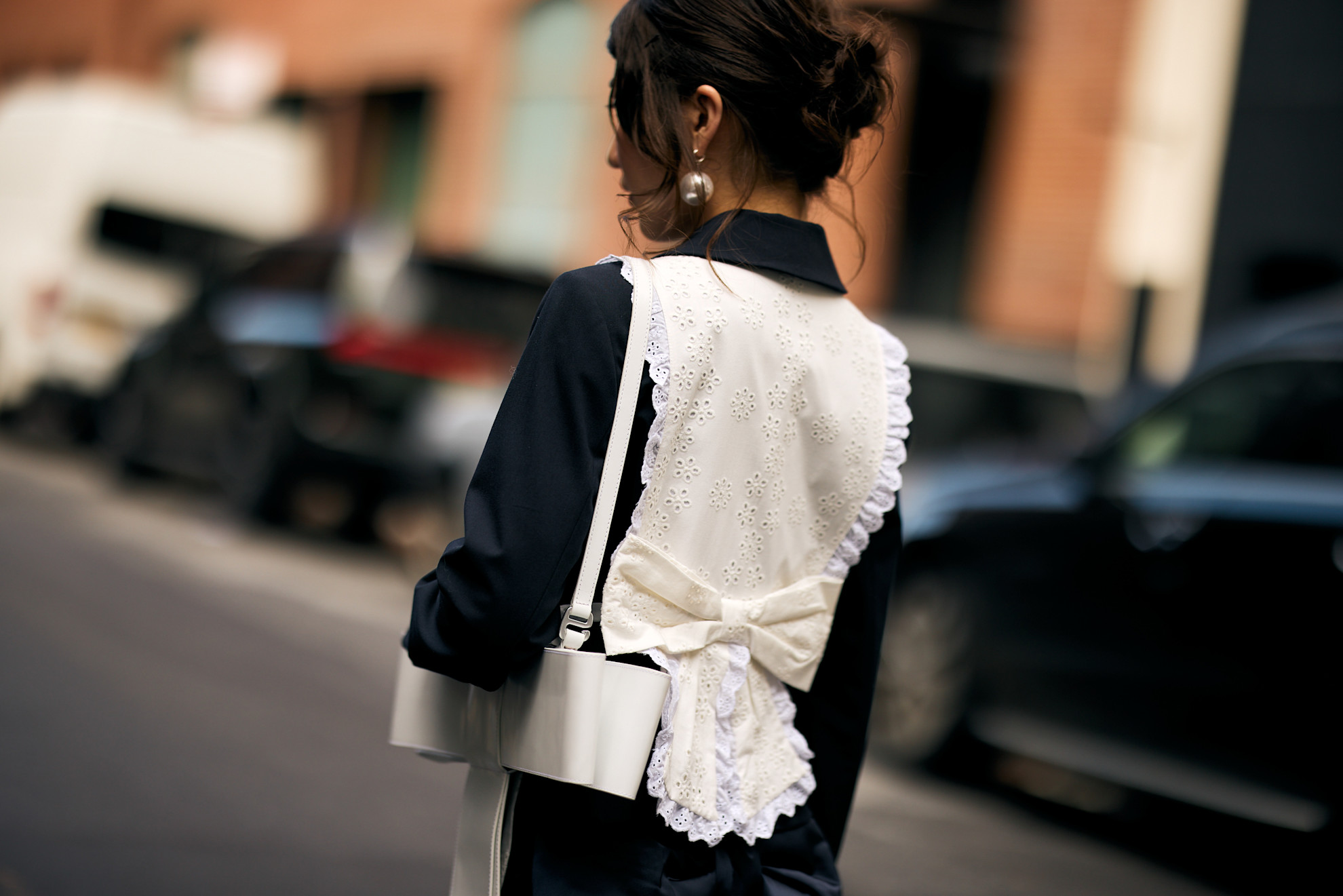 a woman short from the back in a black top, white vest, with a brunette bun