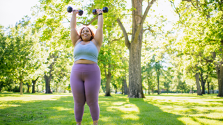 Woman standing outdoors holding two dumbbells