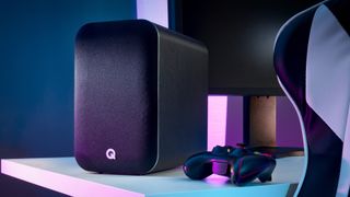 Q Acoustics M20 Bluetooth speaker on desk next to gaming controller with mood lighting