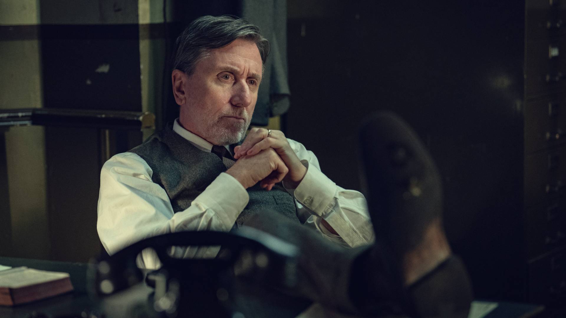 Tim Roth as Beckett reading with his feet on a desk in Peaky Blinders: The Immortal Man
