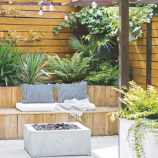Brown garden fence with lush green planys and a modern wood patio seating area.