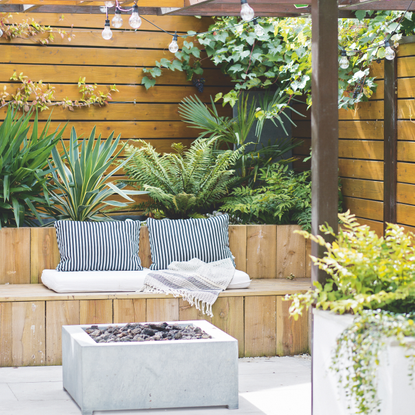 Brown garden fence with lush green planys and a modern wood patio seating area.
