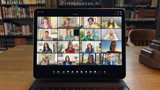 An iPad on a video call with a grid of people, on the backdrop of a library