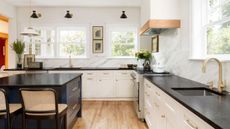 A large kitchen with white cabinets, a black island, marble backsplash, and layered lighting