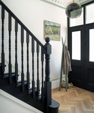 Staircase paint ideas by Paint & Paper Library using black paint on banister and stair treads, black front door, wooden Herringbone flooring and coat stand