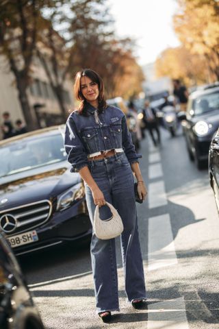 woman at fashion week in the street wearing a cropped denim jacket and denim pants with a white back and black shoes