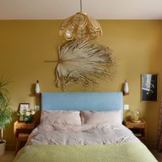 A mustard yellow-painted bedroom with a bed headboard upholstered in baby blue and with soft pink bed linen