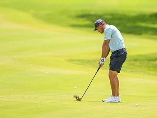Bryson DeChambeau hitting a golf shot with the ball above his feet at Valderrama Golf Club