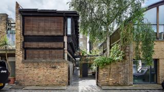 The front of a timber clad house with a brick wall running along the side