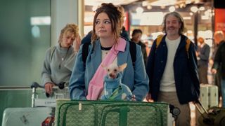 Meg Stalter pushing her suitcase and dog on an airport luggage trolley in a scene from Netflix's "Too Much"