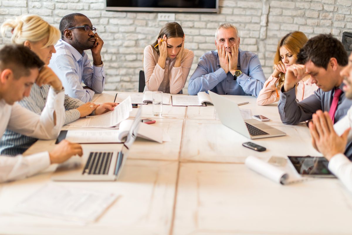 Stressed out office workers sitting around a table with dejected facial expressions.