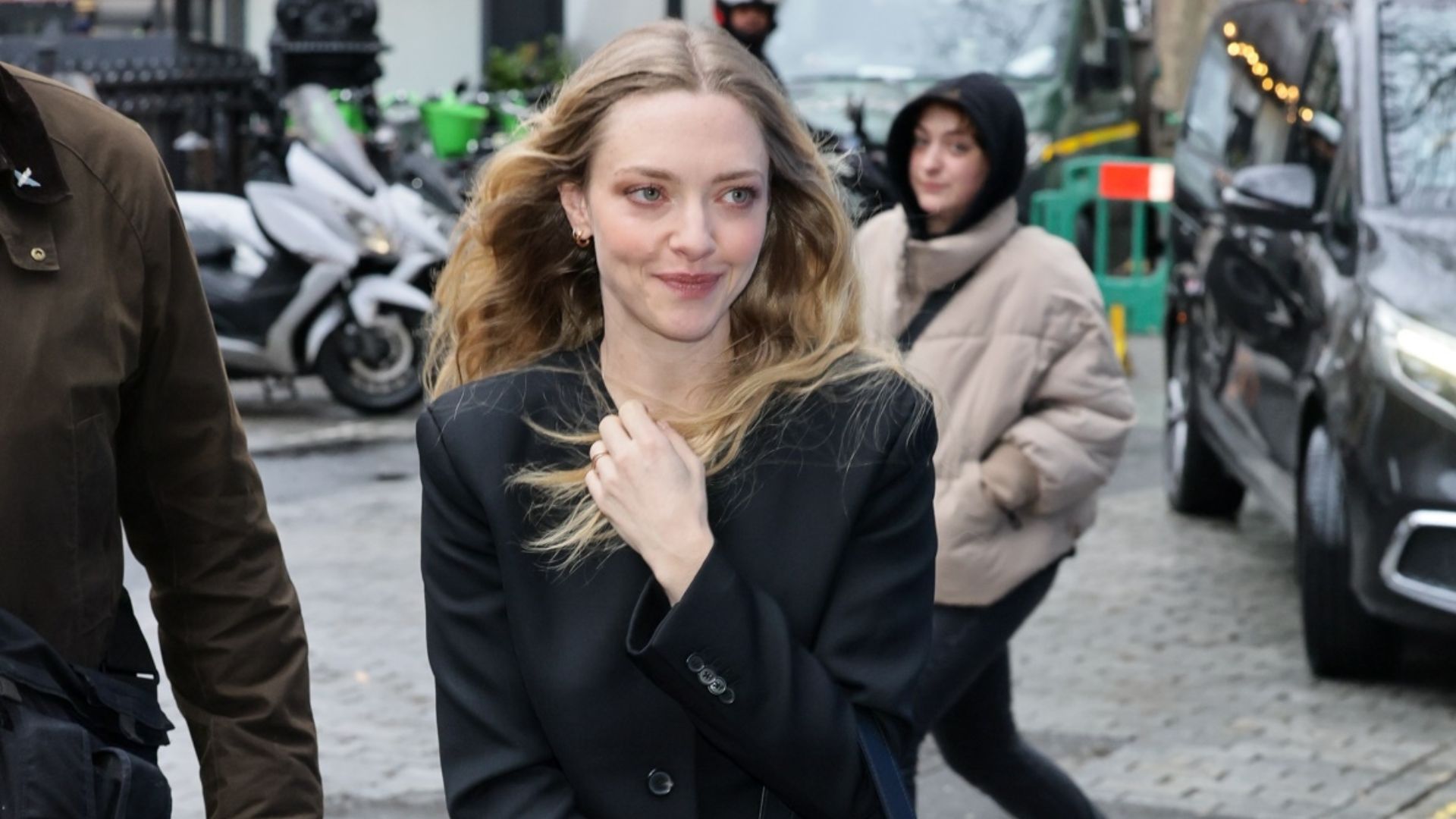 Amanda Seyfried walks outside in London wearing two-tone jeans with a black collarless blazer and black pointed-toe shoes.