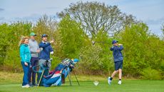 A group of golfers on the tee watch one of their number tee off