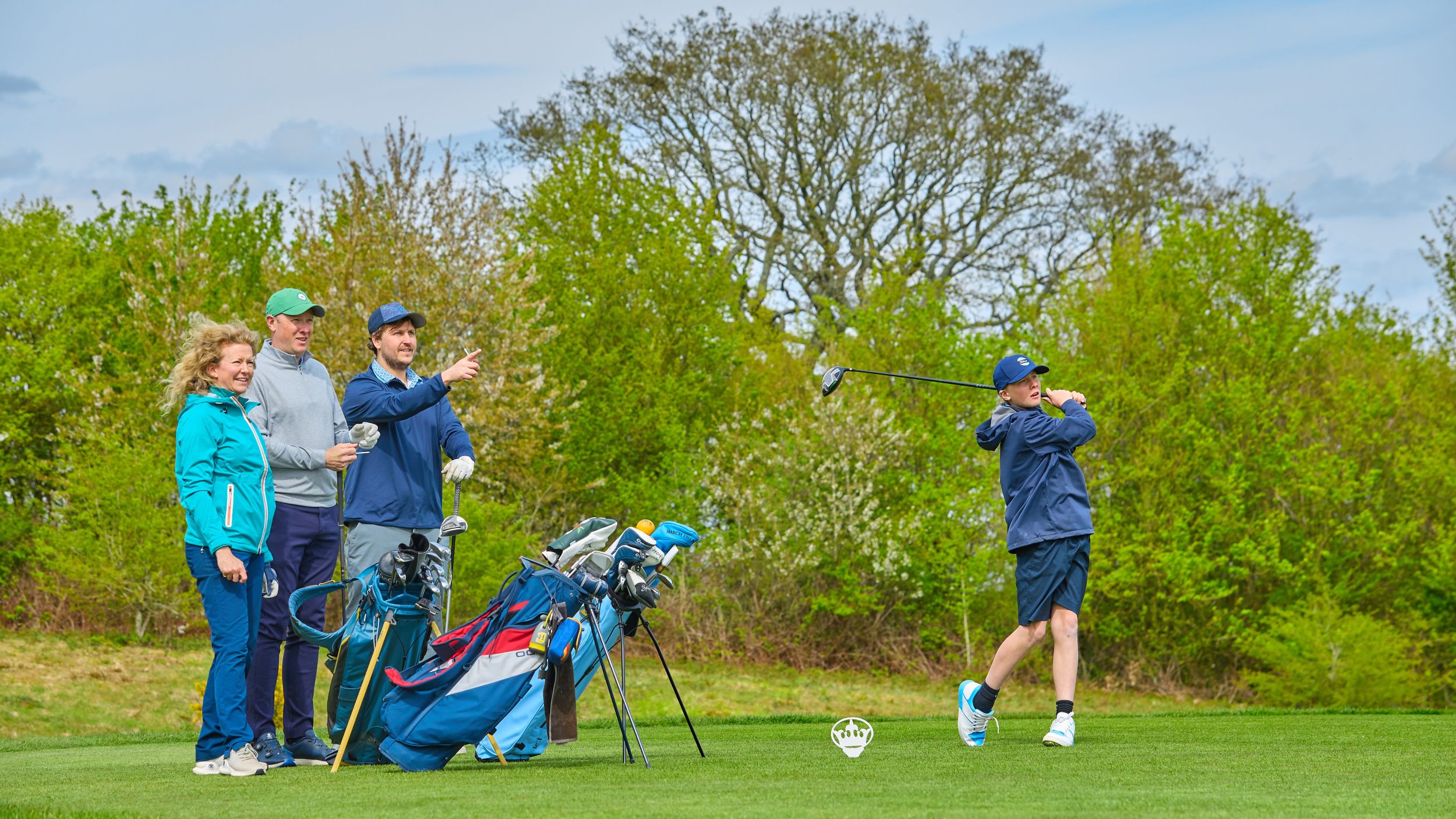 A group of golfers on the tee watch one of their number tee off
