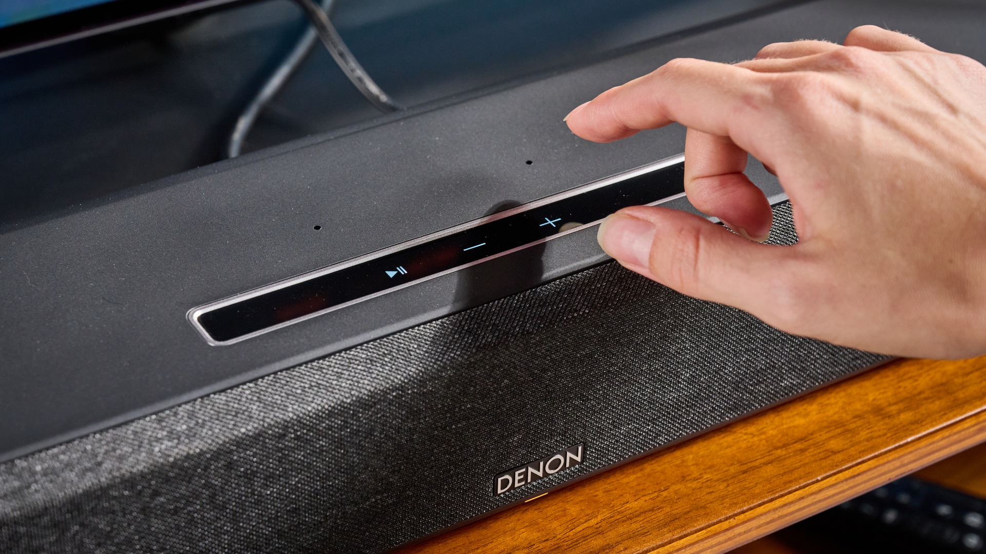 the denon home sound bar 550 with a gray mesh casing and touch controls for bluetooth on the top with a remote and smart home integration