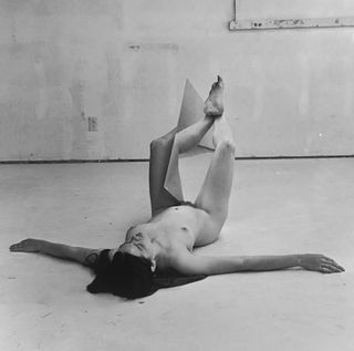 A nude woman lying on her back holding a large mirror with her legs.