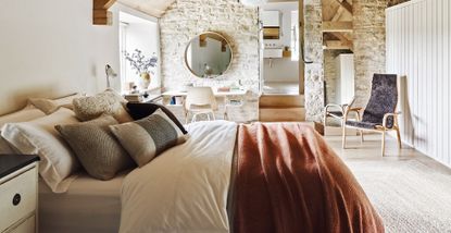 Barn conversion bedroom with exposed stone walls and luxury bedding with lots of pillows to show how to make your bedroom feel like a luxury hotel